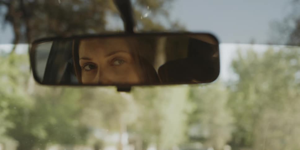A woman driving a car looks in the rearview mirror