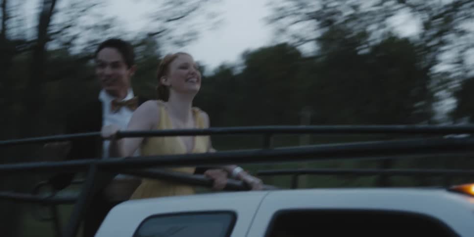 A man and woman in formal wear ride in the back of a truck