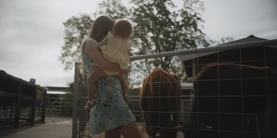 A woman carries a baby past some farm animals