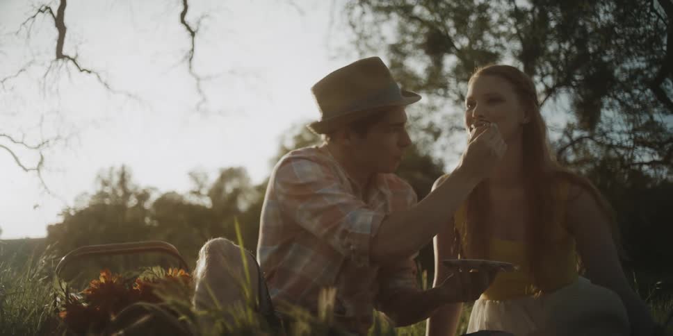 A man draws on a woman's face under a tree
