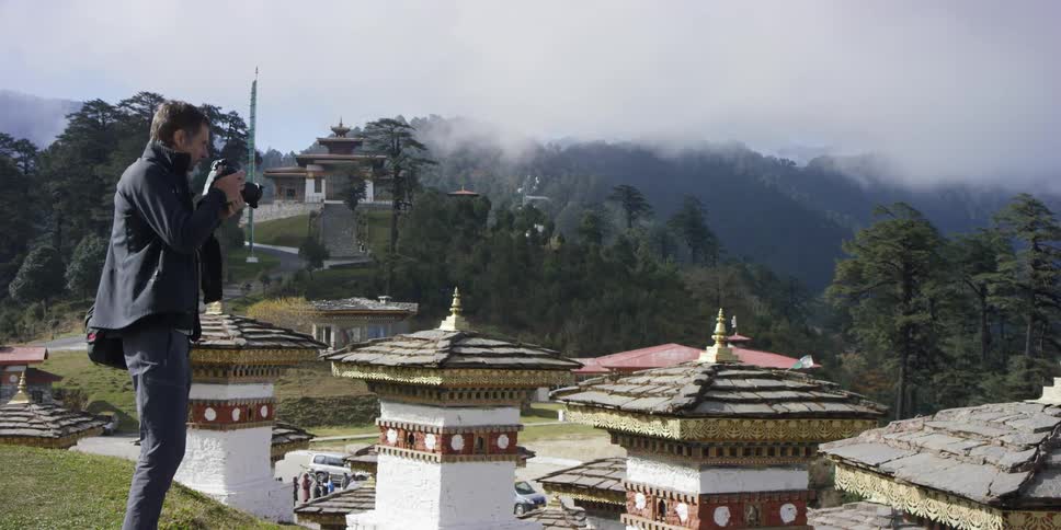 A man is photographing a temple from a hillside