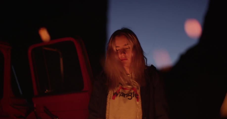 A woman is looking down at a campfire at dawn
