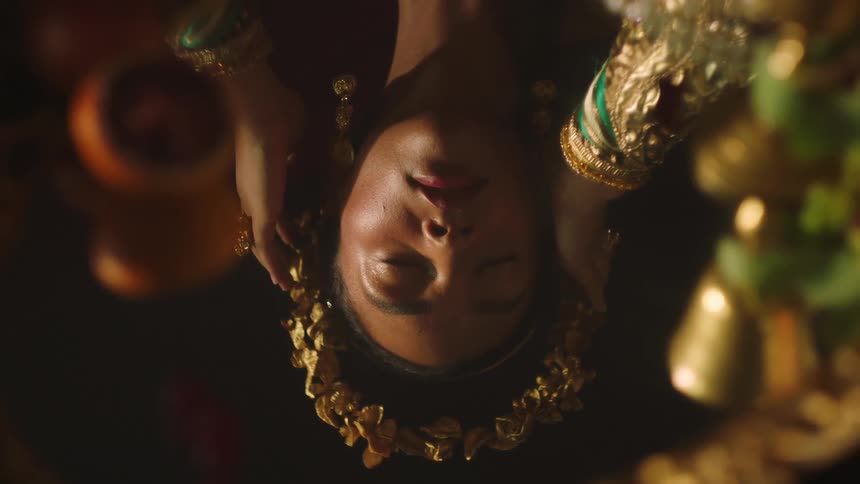 A woman in an elaborate gold outfit adjusts a golden wreath on her head