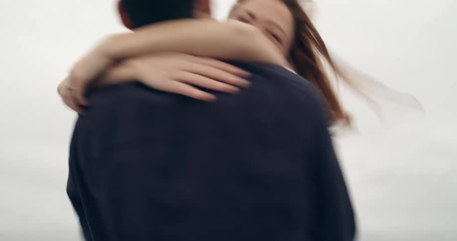 Woman and man run towards each other on the beach and go into each others arms and spin around as they hug