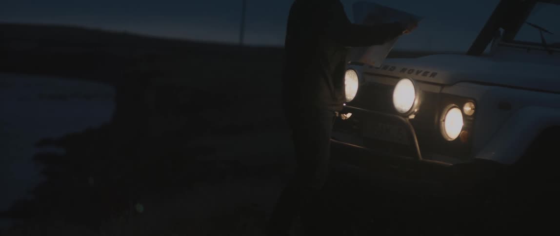 A man uses the headlights on his truck to look at a paper map