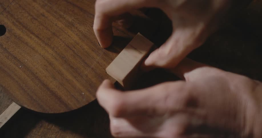 A man places a piece of wood on a string instrument as he builds it