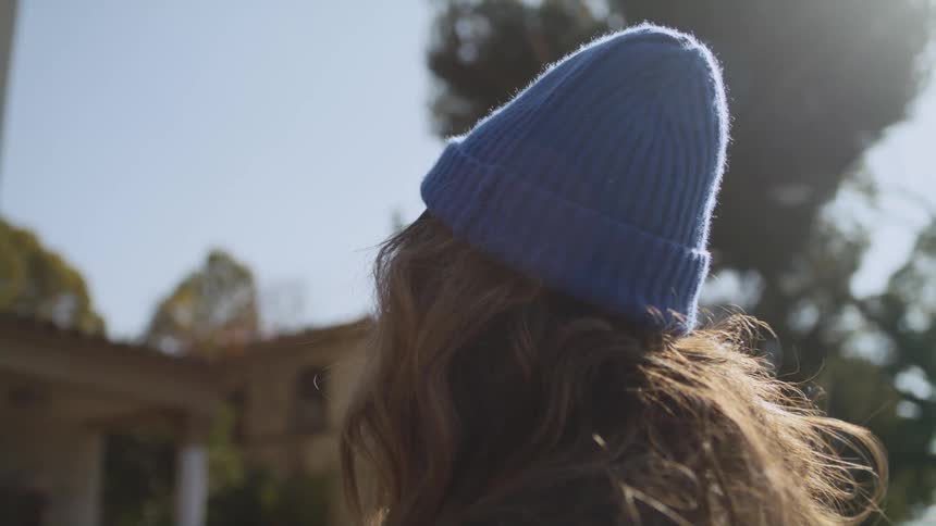 Woman with blue woolly hat and brown wavy hair looks at buildings