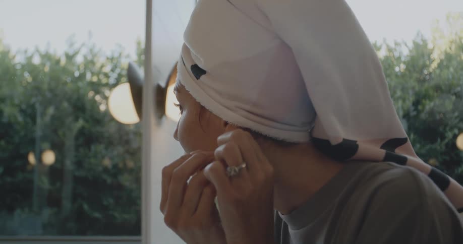 A woman looks in the mirror and puts on earrings