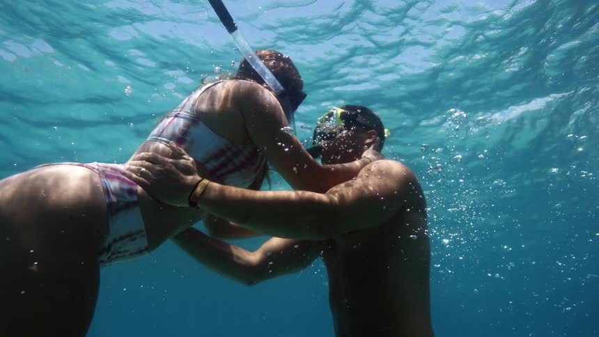 A woman swims into her husbands arms as she begins to surface from snorkeling