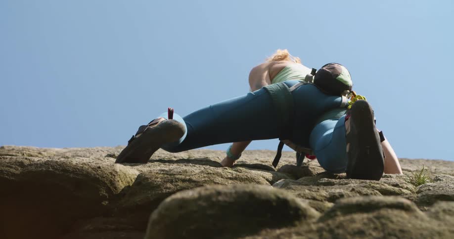 A female rock climber carefully maneuvers up the side of a rocky cliff
