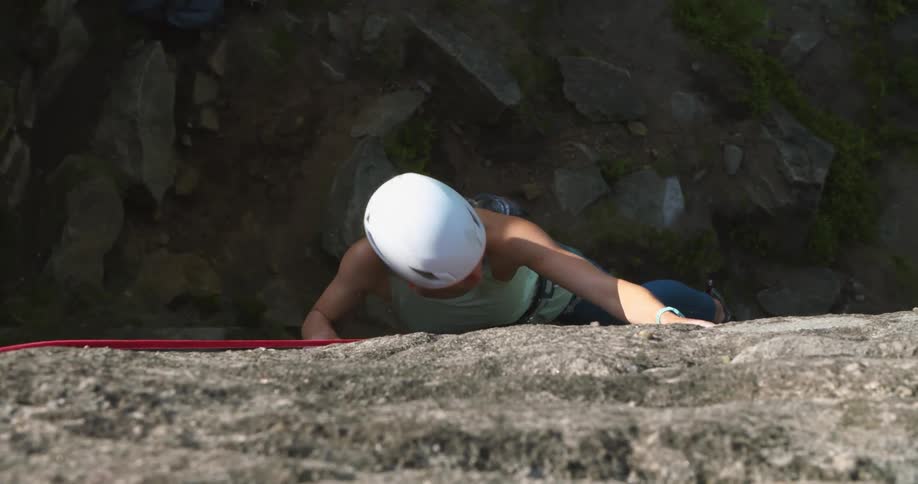 Woman with white helmet green sleeveless shirt and jeans climbs cliff
