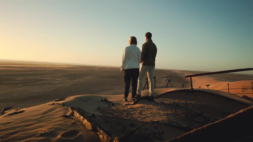 Two people look out peacefully over windy desert