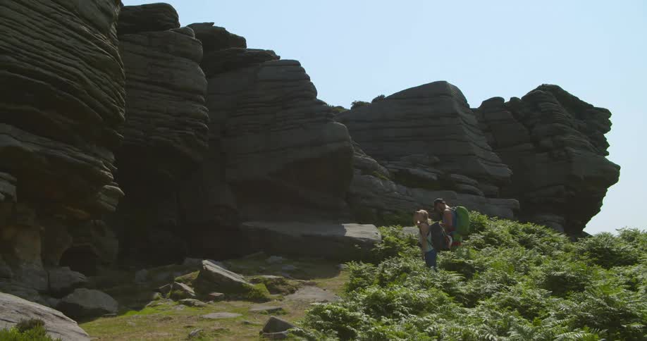Man and woman with backpacks stand in long grass reading map looking at cliffs