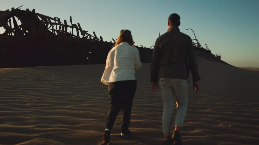 Man and woman walk towards an amazing desert shipwreck with excitment