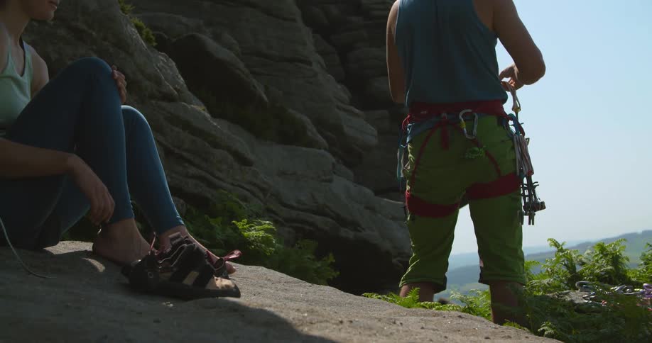 A woman takes off her sandals while sitting below a rock wall as she and friends go rappelling