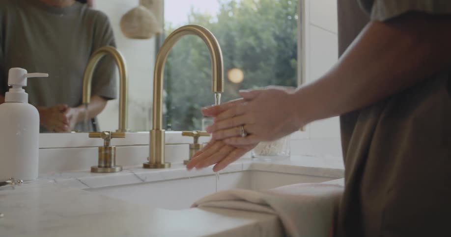 Woman with green t shirt and rings washes hands under tap in the bathroom