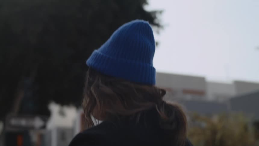 Woman wearing a blue toque walks past the trees and buildings in the city on a cloudy day