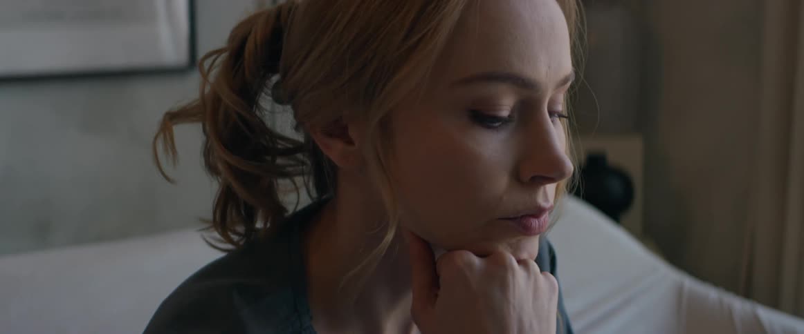 A woman is sitting on a bed and contemplating