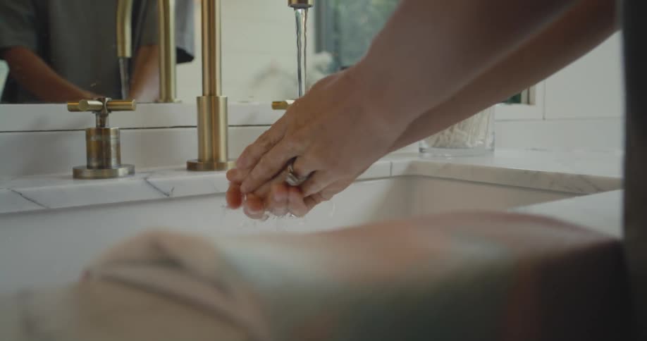 A woman stands over a bathroom sink while thoroughly washing her hands
