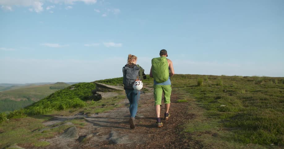 A man and woman carry rope as they hike along the top of a hill