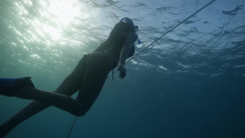 Female snorkeler follows line tied to pole in seafloor up toward surface