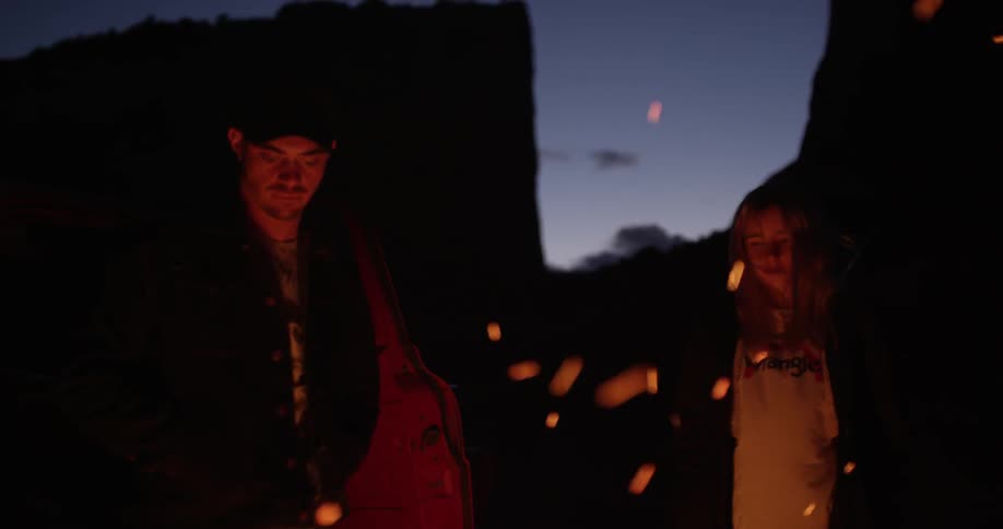 A man and woman stand before a campfire at dawn