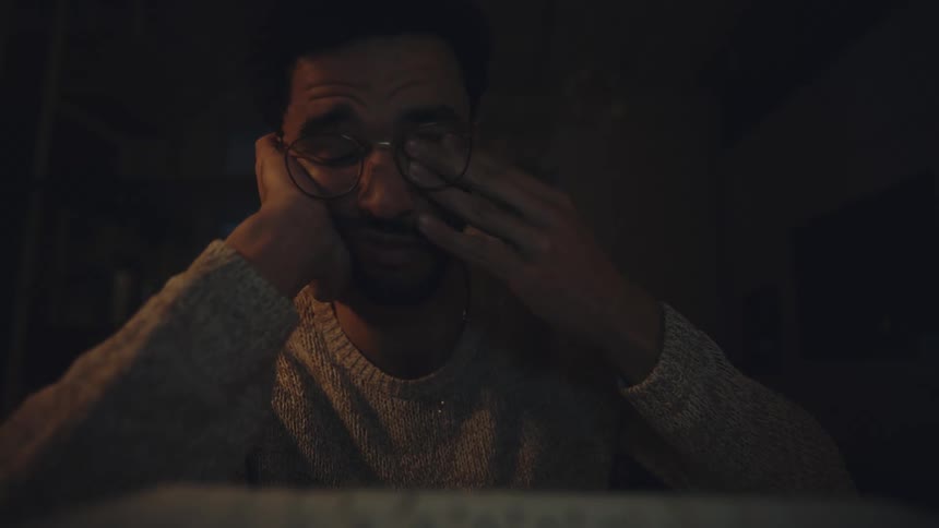 Exhausted worker types on computer stopping to rub his eyes