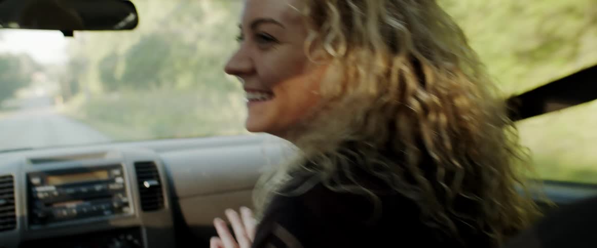 Blonde female passenger in a car smiles and laughs as she talks to the driver on a sunny day