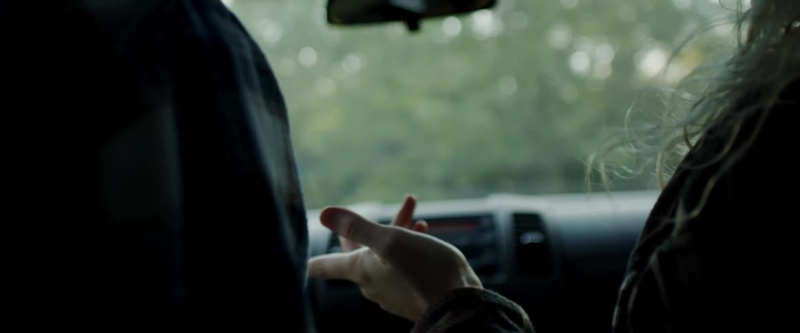 Young blonde woman sitting on the passenger seat of a driving car gesturing with her hands