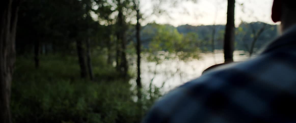 Woman wearing a cowboy hat laughs while standing in a forest next to a man near the lake