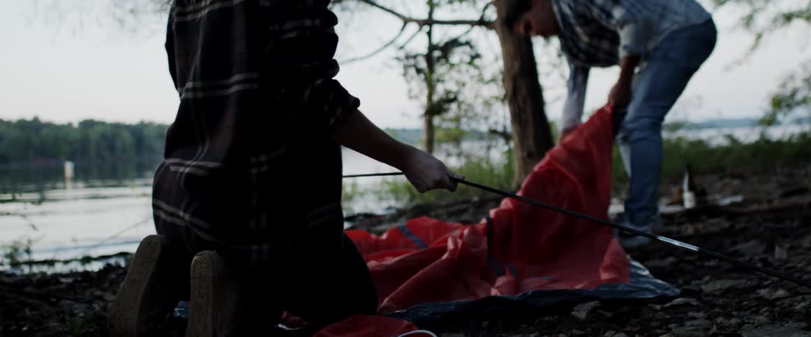 Man and woman set up tent on riverbank