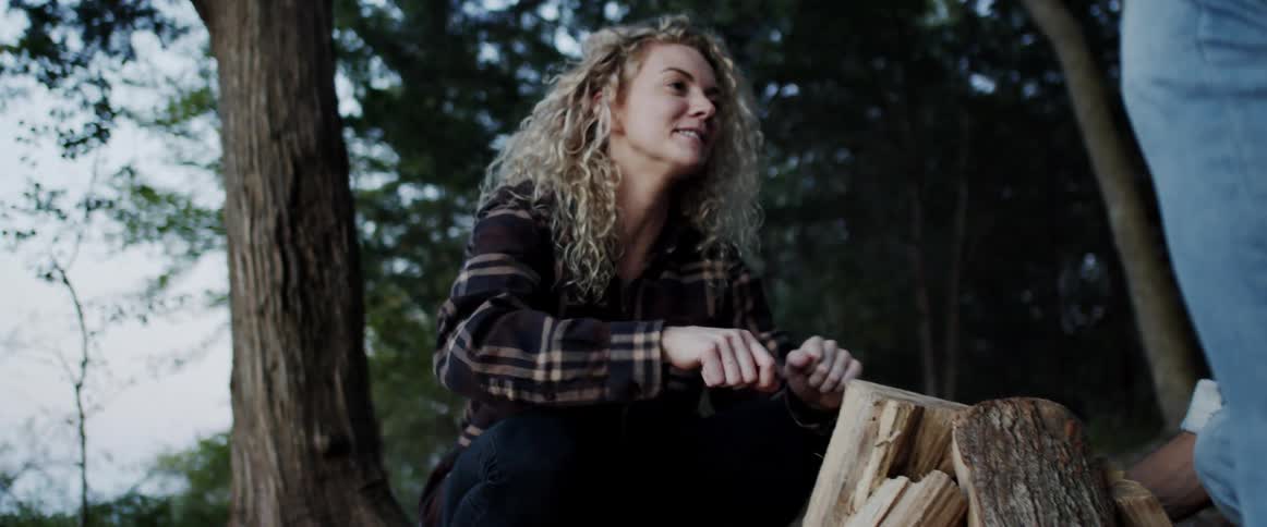 A woman and man stack firewood in preparation to start a campfire outdoors during the day
