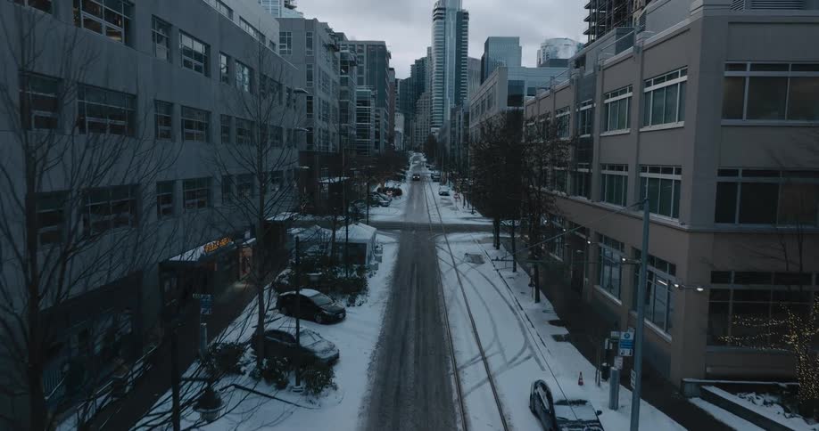 Aerial view of a downtown street with tall buildings and snow on the road as a few people are walking and a street car travels by
