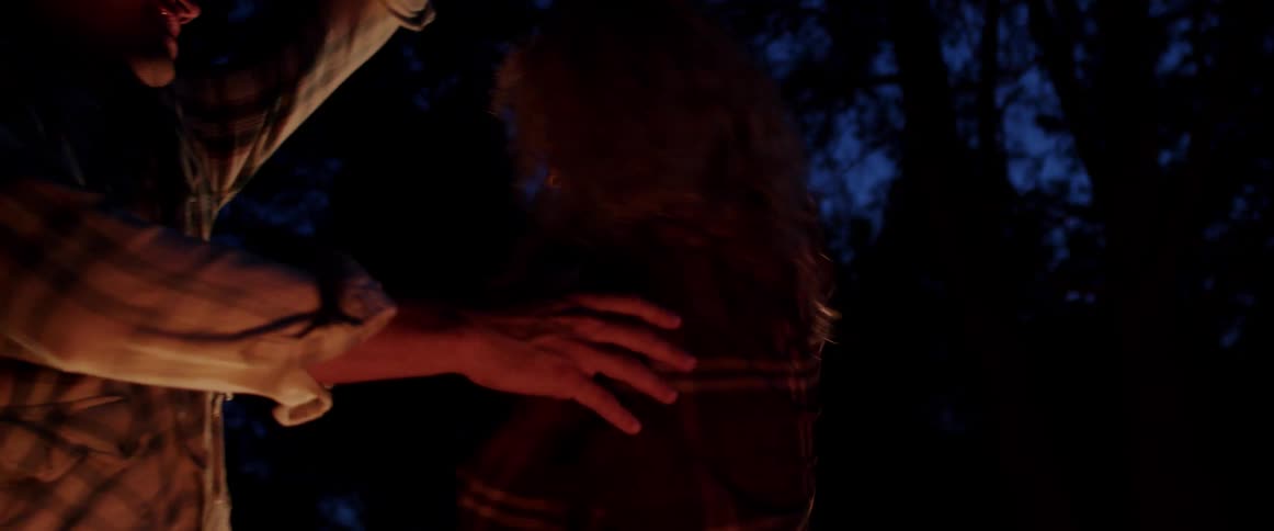 A woman and man dance by the light of a campfire outdoors at night