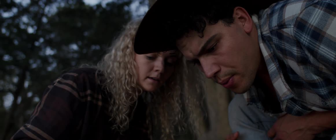 Man and woman carefully start campfire outdoors in forest