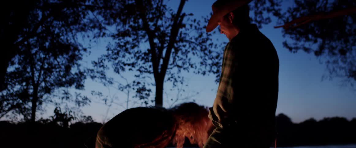 Man wearing a cowboy hat pretends to be shooting a gun as a woman laughs while holding a bottle of wine