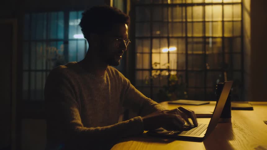 Time lapse of a young man sitting at a desk  working on a laptop at night
