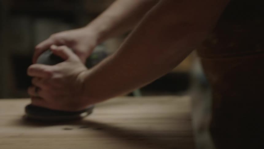 A man wearing a green shirt sands a block of wood