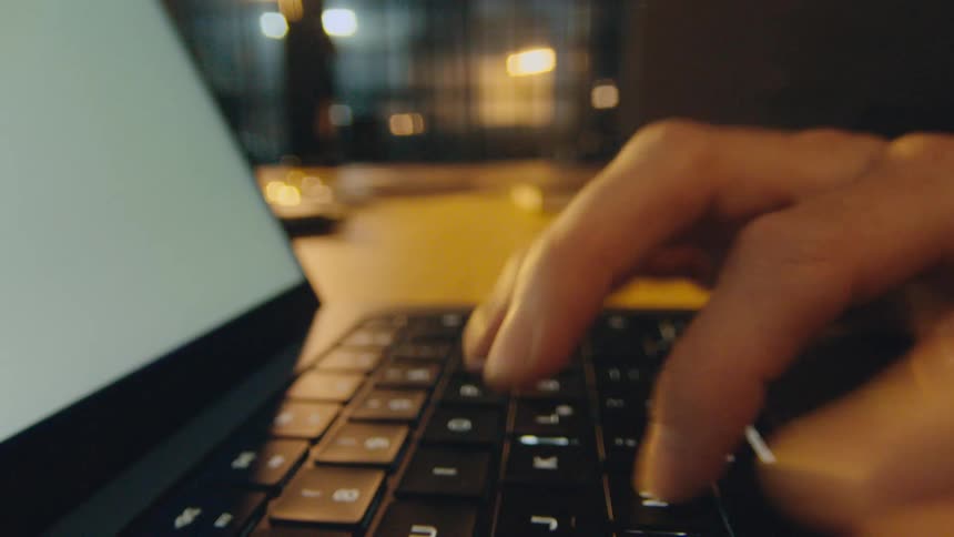 camera moves through hands and fingers typing on a laptop keyboard