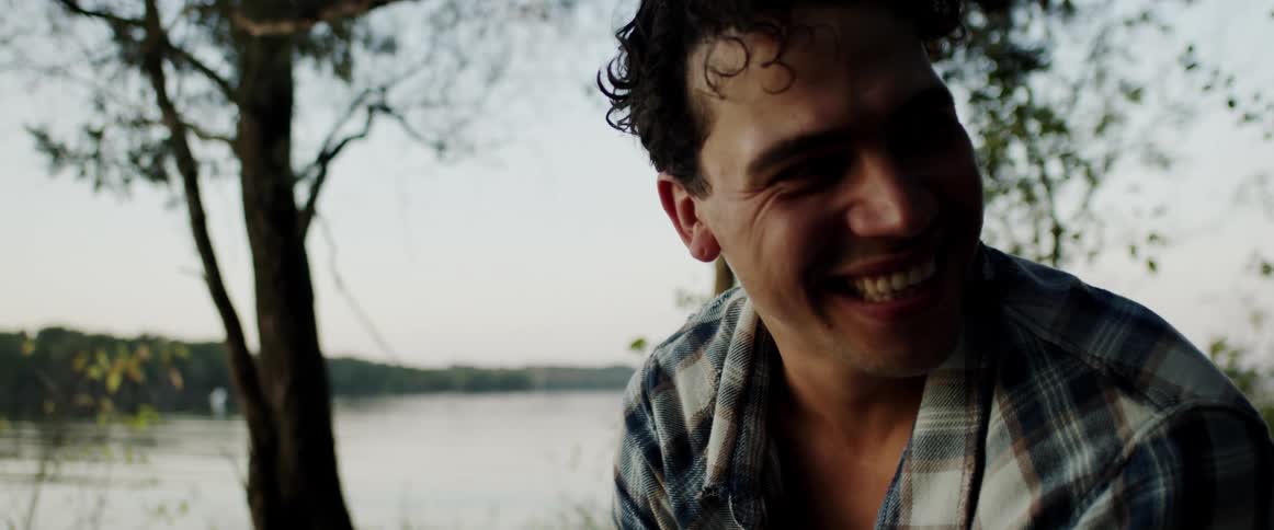A man laughs while sitting on a riverbank during the day