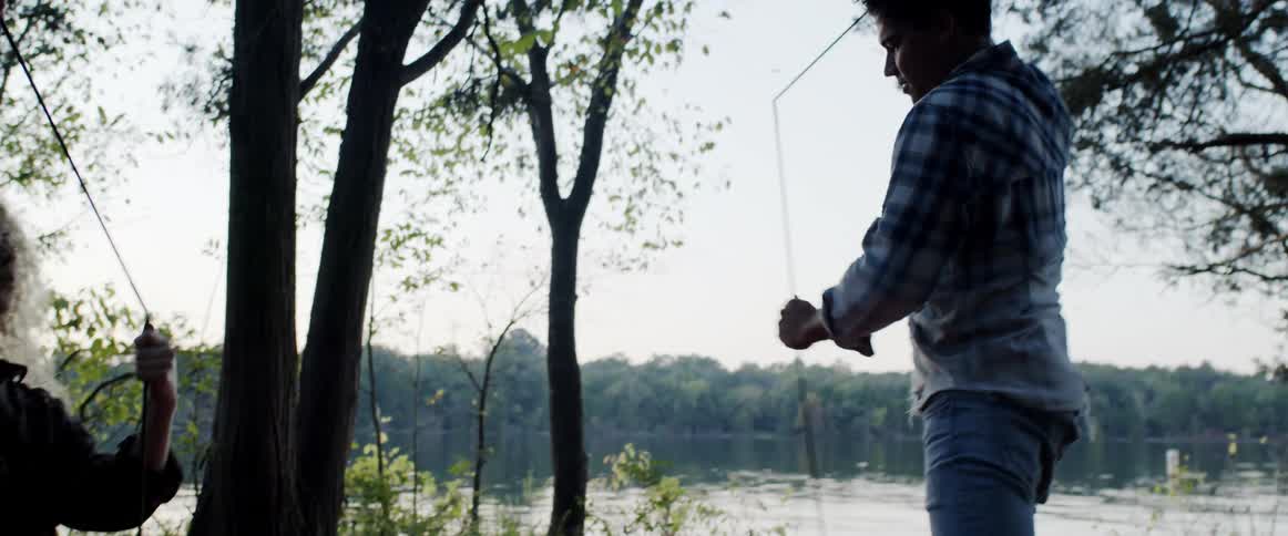 A man and woman put together tent poles by a lake