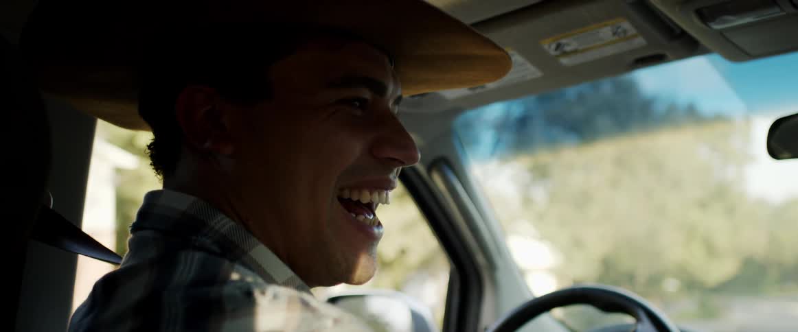Male driver wearing cowboy hat laughs as he talks with passenger