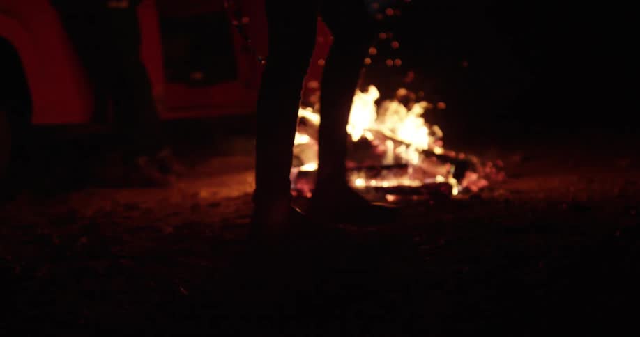 A person walks past a campfire at night
