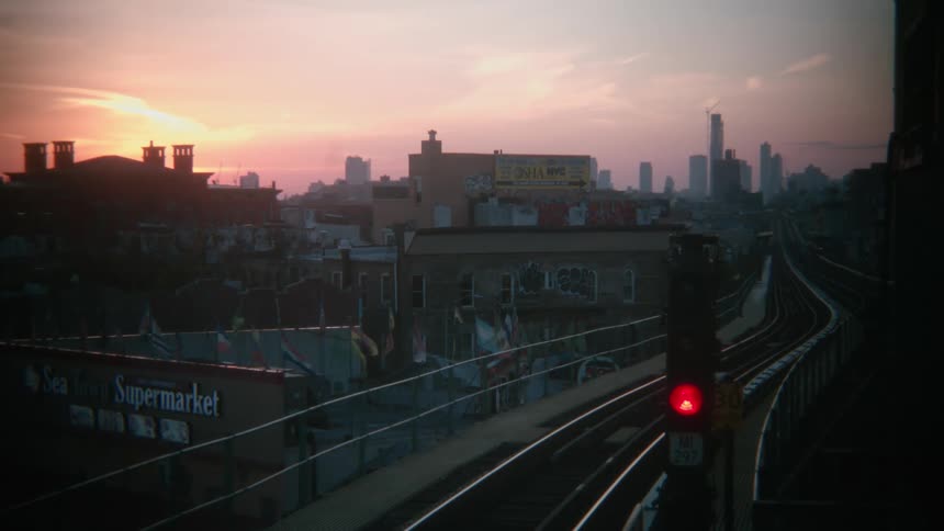 Train tracks flow along past supermarket heading toward downtown skyline under a red sky