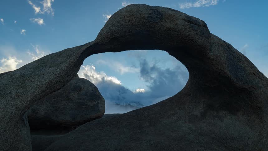 Clouds break up and move showing a mountain through the mobius arch loop