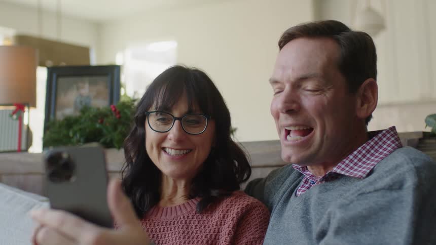 A man and his wife sitting on the couch having a video call with family looking sentimental
