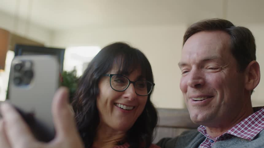 A man holds a smartphone while participating in a video chat alongside a woman sitting beside him