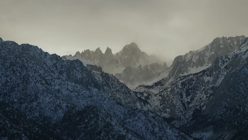 Speed up time lapse of clouds rolling over the snow covered slopes of a mountain range