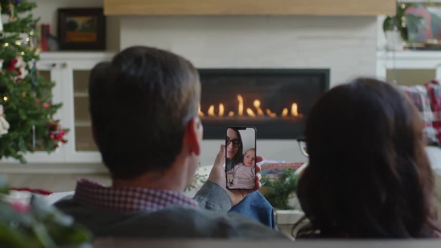 A man and woman use a smartphone to video chat with a woman holding a baby
