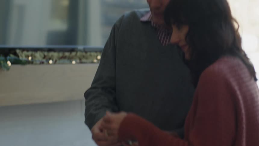 A husband and wife smile at an ornament before hanging it on the tree